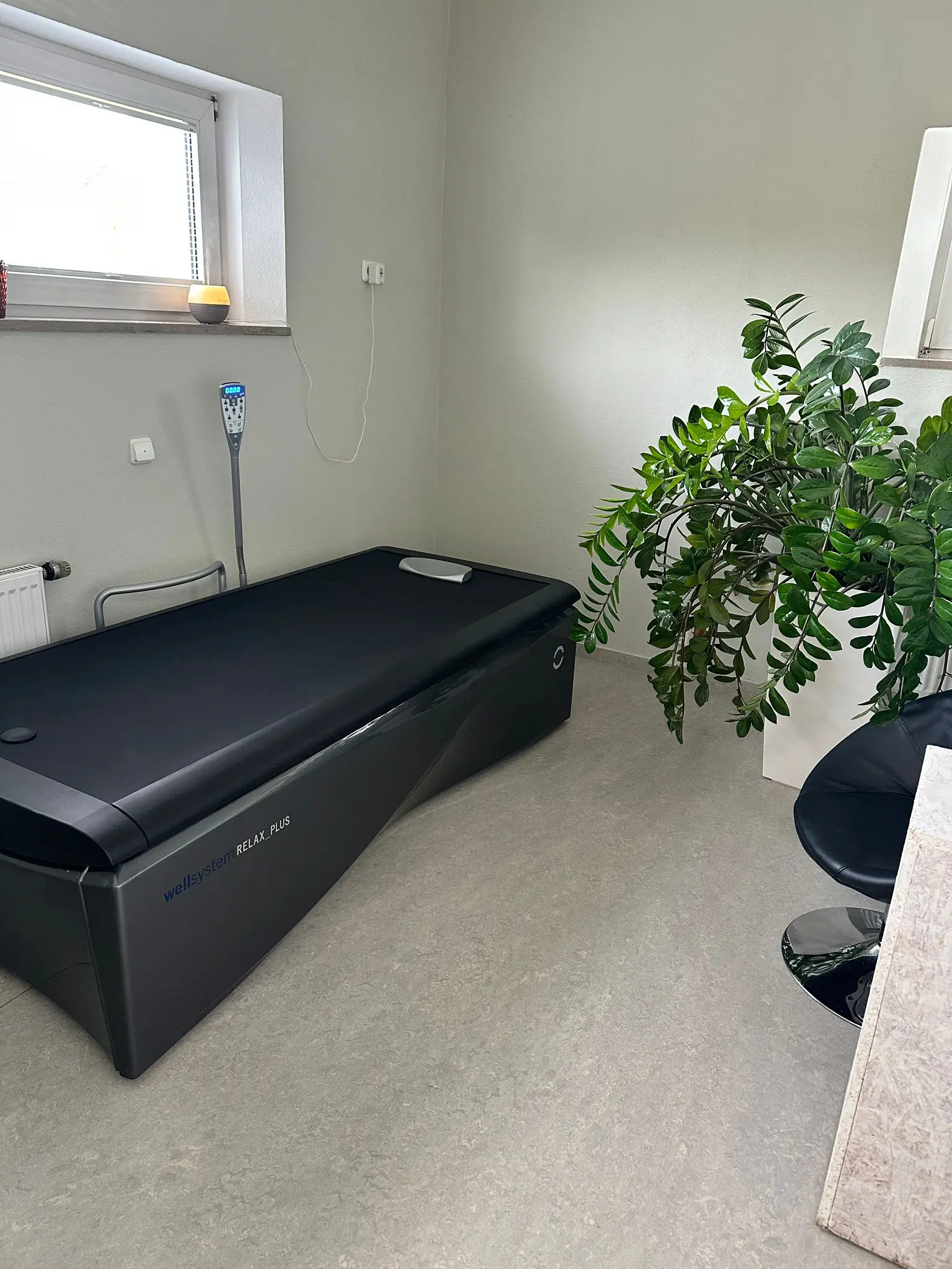 Ein elegantes schwarzes Hydromassagebett steht in einem minimalistischen Raum mit hellen Wänden, einer großen Blattpflanze, einem modernen schwarzen Stuhl und einem Fenster, das Tageslicht hereinlässt. Ein elegantes schwarzes Hydromassagebett steht in einem minimalistischen Raum mit hellen Wänden, einer großen Blattpflanze, einem modernen schwarzen Stuhl und einem Fenster, das Tageslicht hereinlässt.